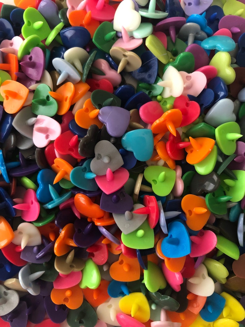 Puede incluir: Un gran surtido de botones de pl&aacute;stico en forma de coraz&oacute;n de varios colores. Los botones son de varios tonos de rojo, naranja, amarillo, verde, azul, morado, rosa y blanco.