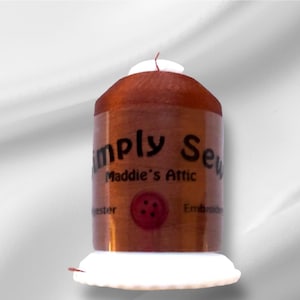 Peut inclure: Une bobine de fil à broder en polyester de couleur cuivre avec l'étiquette "Simply Sew Maddie's Attic" et les mots "Embroidery Thread" et "Polyester" visibles.