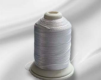 May include: A spool of white thread on a white plastic bobbin. The thread is wound tightly and has a slight sheen.
