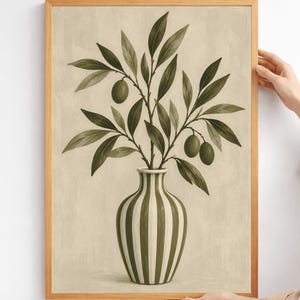 Op de afbeelding: Een ingelijste kunstprint met een verticale olijftak met groene bladeren en drie olijven in een gestreepte vaas. De vaas heeft afwisselende verticale strepen in crème en olijfgroen. De achtergrond is een getextureerde, neutrale beige kleur.