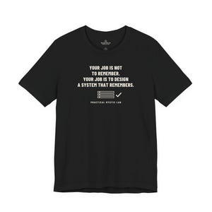 May include: A black short-sleeved t-shirt featuring white text that reads: YOUR JOB IS NOT TO REMEMBER. YOUR JOB IS TO DESIGN A SYSTEM THAT REMEMBERS. Below the text is a graphic of a list with a checkmark and the words PRACTICAL MYSTIC LAB.