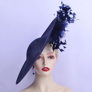 May include: A navy blue hat with a wide brim and a decorative cluster of feathers. The hat has an asymmetrical design and is likely made of woven fabric. The text "Labellemoi" is visible on the lower right.