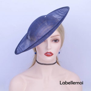 May include: A wide-brimmed hat in a deep blue color, made of a woven material. The hat is tilted at an angle, and the brim is slightly curved. The hat is worn by a mannequin with blonde hair.