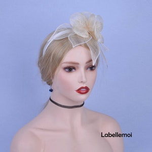 May include: A white headband with a large, ivory-colored flower made of netting. The headband is worn on a mannequin with blonde hair.