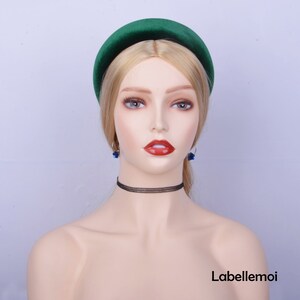 May include: A wide green velvet headband with a slightly rounded shape. The headband is worn on a mannequin with blonde hair and blue earrings.