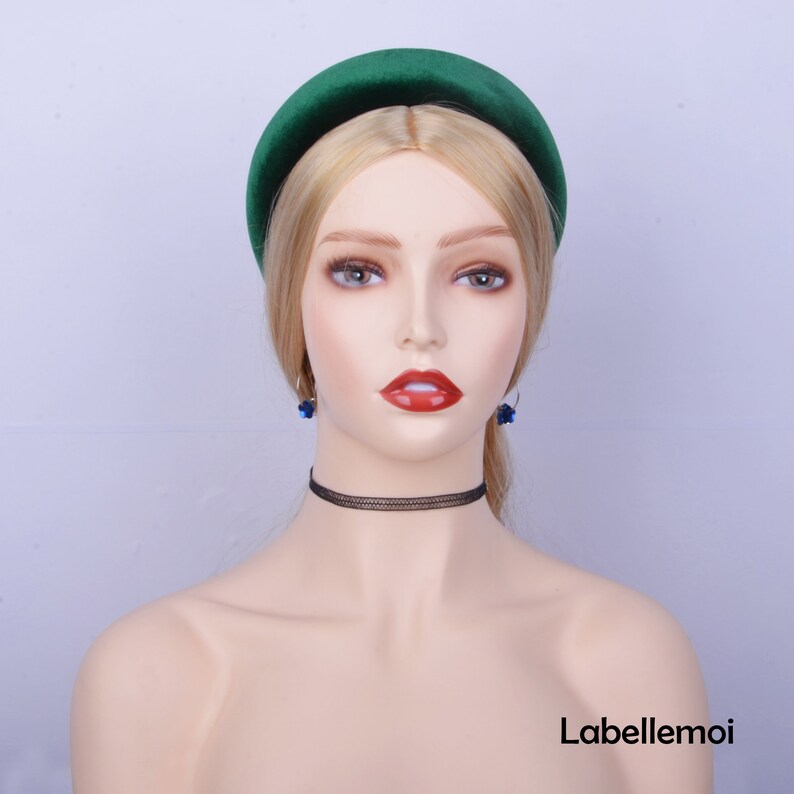 May include: A wide green velvet headband with a slightly rounded shape. The headband is worn on a mannequin with blonde hair and blue earrings.