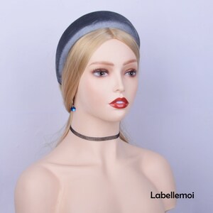 May include: A gray velvet headband with a wide, padded band. The headband is worn on a mannequin with blonde hair.