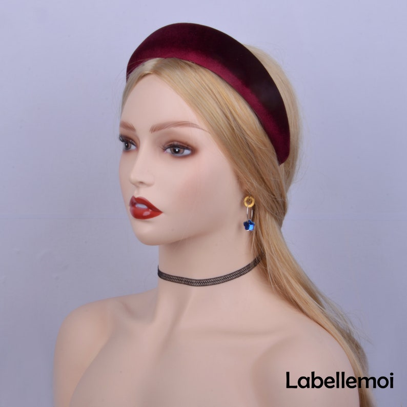 May include: A wide, burgundy velvet headband for women. The headband is made of a soft, plush velvet fabric and has a simple, elegant design.