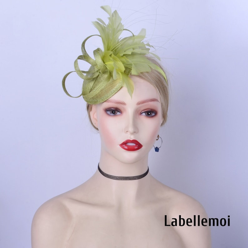 May include: A green fascinator hat with feathers and a small round base. The hat is worn on a mannequin's head.