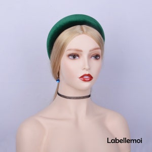 May include: A dark green velvet headband with a wide, padded band. The headband is worn on a mannequin with blonde hair.