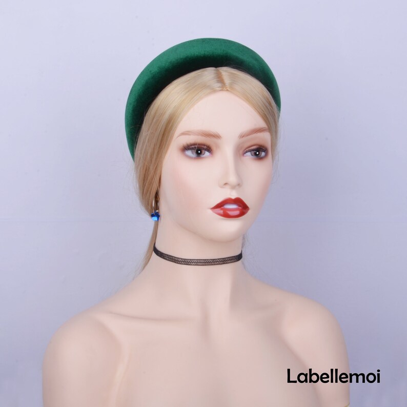 May include: A dark green velvet headband with a wide, padded band. The headband is worn on a mannequin with blonde hair.