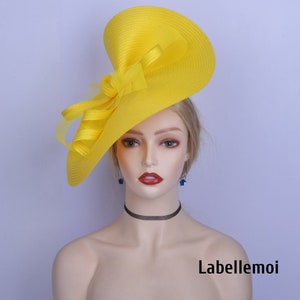 May include: A bright yellow wide-brimmed hat with a large bow. The hat is made of a straw-like material and has a slightly angled brim. The hat is worn on a mannequin's head.