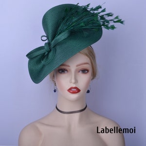May include: A green fascinator hat with a large bow and feathers. The hat is made of a straw-like material and has a wide brim.