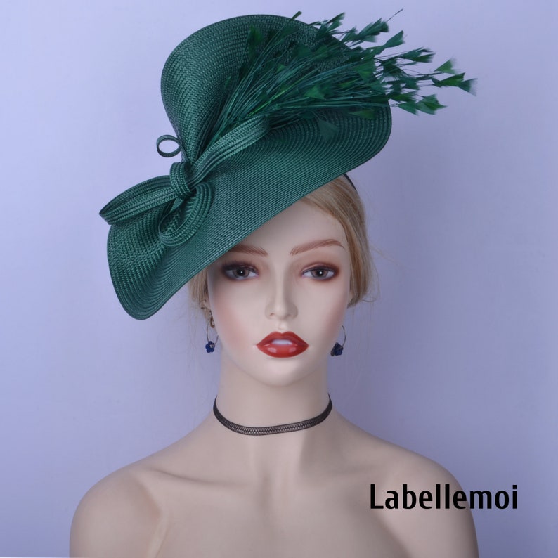 May include: A green fascinator hat with a large bow and feathers. The hat is made of a straw-like material and has a wide brim.