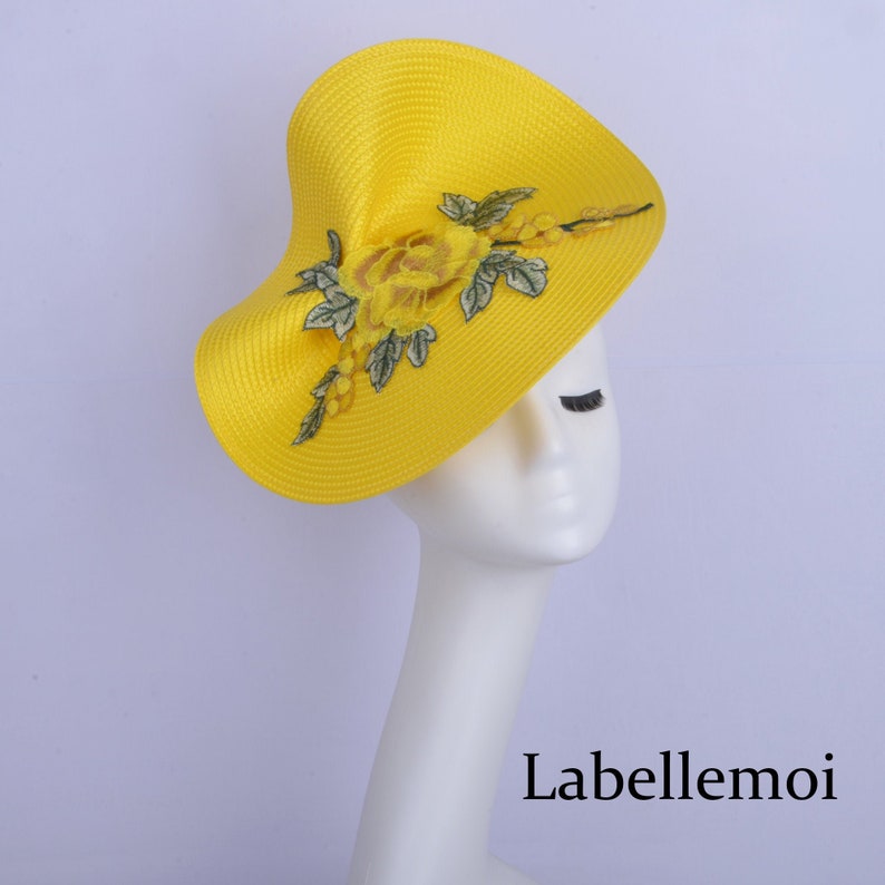 May include: A bright yellow hat with a large, yellow flower and green leaves embroidered on the front. The hat is made of a straw-like material and has a wide brim.