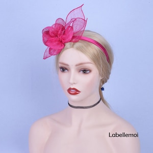 May include: A pink fabric flower headband with a satin band. The headband is worn on a mannequin with a light blue background.