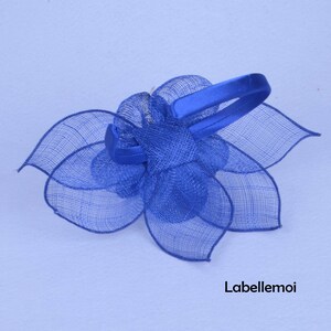 May include: A blue flower hair clip with a satin headband. The flower is made of a delicate mesh fabric.