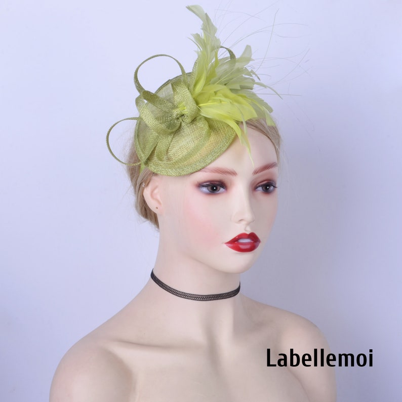May include: A green and yellow feathered hat with a small round base. The hat is worn on a mannequin's head. The text "Labellemoi" is visible in the bottom right corner of the image.