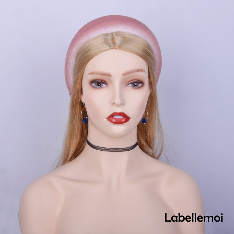 May include: A wide, pink velvet headband with a slightly ombre effect. The headband is worn on a mannequin with blonde hair.