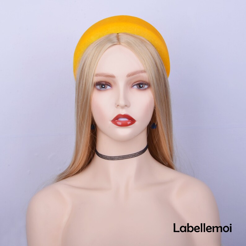 May include: A yellow velvet headband with a rounded shape. The headband is worn by a mannequin with blonde hair.