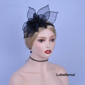 May include: A black headband with a large black flower made of netting. The flower has a layered design and is positioned on the left side of the headband.