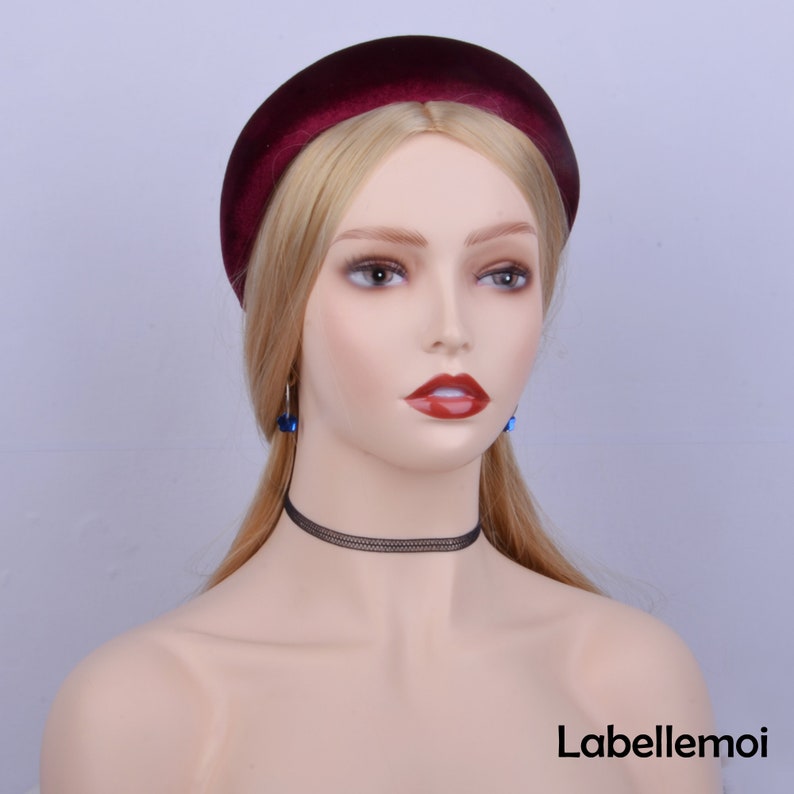 May include: A woman wearing a wide, burgundy velvet headband. She is also wearing a black choker necklace and blue earrings.