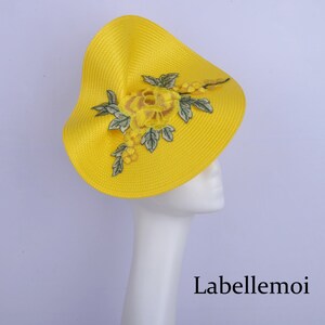 May include: A bright yellow hat with a large yellow flower and green leaves embroidered on the side. The hat is on a white mannequin head. The text "Labellemoi" is visible at the bottom of the image.