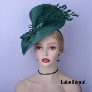 May include: A green fascinator hat with a large, wide brim and a bow on the side. The hat is decorated with green feathers.