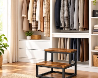May include: A two-step stool featuring a dark brown wood-grain finish on the treads and a sturdy black metal frame. The stool is positioned in front of a white closet filled with hanging coats, blazers, and trousers on wooden hangers.