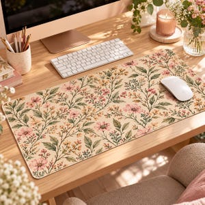 Op de afbeelding: Een rechthoekige bureaumat met een crèmekleurige achtergrond en een herhalend botanisch patroon van roze bloemen, kleine gele bloesems en groene bladeren. De mat heeft een glad oppervlak en ligt op een houten bureau onder een computer.