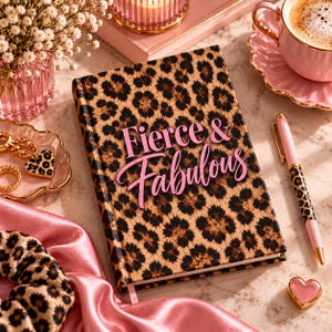 Può includere: Un taccuino con copertina rigida con motivo leopardato marrone e nero che riporta la scritta Fierce & Fabulous in corsivo rosa. Il taccuino è accompagnato da una penna abbinata con motivo leopardato e dettagli rosa e un accessorio in raso rosa.