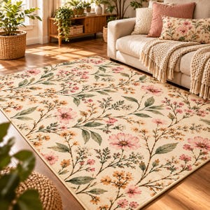May include: A rectangular area rug featuring a cream-colored background with a repeating botanical pattern of pink flowers, small yellow blossoms, and muted green leaves spread across the surface in a flowing, vine-like arrangement.