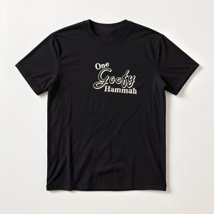 May include: A black short-sleeved t-shirt featuring the white text One Goofy Hammah printed on the upper chest area. The shirt has a crew neckline and a standard fit, with the graphic design centered in a stylized script and serif font combination.