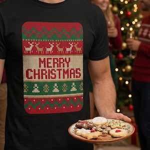Op de afbeelding: Een zwart t-shirt met een rechthoekige afbeelding in een gebreide stijl met rode, groene en beige patronen. Het ontwerp bevat rendieren en kerstbomen met de tekst MERRY CHRISTMAS in rode letters op een beige achtergrond.