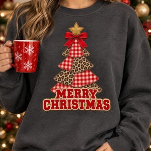 Op de afbeelding: Een donkergrijs sweatshirt met ronde hals en een afbeelding van een kerstboom bestaande uit afwisselende rood-witte vichy-ruitjes en luipaardprint secties. De boom is bekroond met een gouden ster en een rode strik, met de tekst MERRY CHRISTMAS.