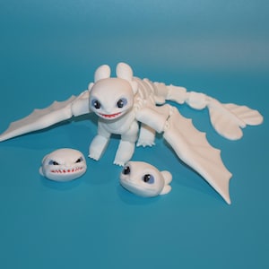 May include: A white articulated dragon figurine with large wings and a long tail, accompanied by two separate smaller white dragon heads. The main figure has large dark eyes and a red mouth, while the two detached heads feature distinct expressions.