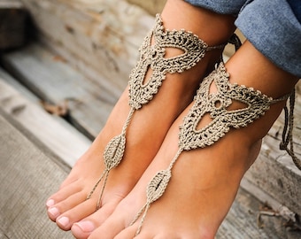 Puede incluir: Un par de joyas de pie de ganchillo con un diseño de hoja. Las joyas están hechas de hilo beige y se llevan en los pies de una persona.