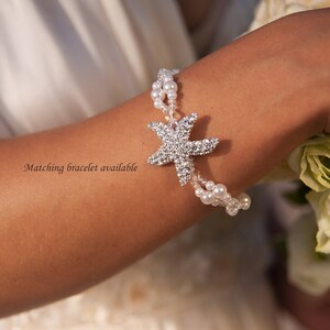 May include: A silver bracelet with a starfish charm. The starfish is encrusted with small, sparkling crystals. The bracelet also features strands of small, white pearls. The text "Matching bracelet available" is visible.