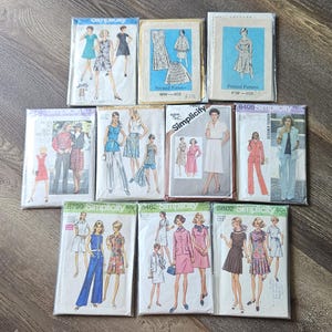 May include: A collection of eleven vintage Simplicity sewing patterns in clear plastic sleeves, featuring various garment illustrations including dresses, skirts, trousers, and jackets with printed text and model sketches on each individual envelope.