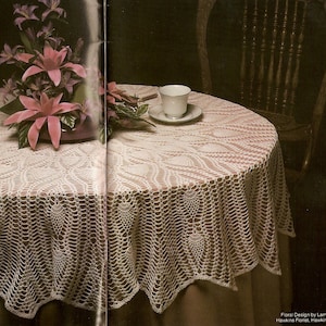 May include: A white crocheted tablecloth with a delicate lace pattern, featuring a scalloped edge. The tablecloth is laid on a table with a cup and saucer on top. The tablecloth is a beautiful and elegant addition to any home.