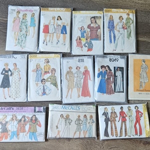 Puede incluir: Una colección de trece sobres de patrones de costura vintage de marcas como Simplicity, Butterick y McCall's. Cada sobre presenta ilustraciones de varios estilos de ropa, incluyendo vestidos, blusas y trajes de pantalón, con nombres de marca y números de patrón impresos.