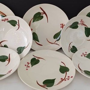 May include: Set of seven white ceramic plates with a green and red ivy leaf design. The plates are in various sizes, including dinner plates, salad plates, and bowls.
