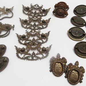 May include: A collection of antique brass cabinet hardware, including drawer pulls, knobs, and handles. The hardware features intricate designs and a worn, aged patina.