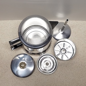 May include: A silver percolator coffee pot with a black handle and a removable lid. The pot is disassembled, showing the filter and other parts.