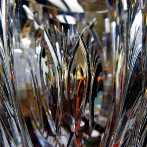 Puede incluir: Primer plano de un jarr&oacute;n de vidrio transparente con intrincados dise&ntilde;os tallados. La luz se refleja en el vidrio, creando un efecto arco&iacute;ris.