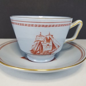 May include: A blue and white teacup and saucer set with a red ship design. The cup has a gold rim and the saucer has a gold band around the edge.
