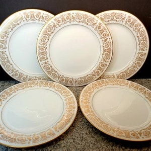 May include: Set of five white dinner plates with a gold rim and intricate gold floral pattern.