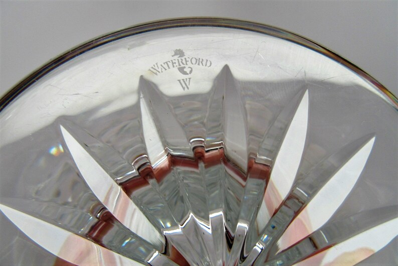 Puede incluir: Primer plano de la parte inferior de una copa de cristal Waterford. La copa tiene un patr&oacute;n de estrella y el logotipo de Waterford est&aacute; grabado en la parte inferior.
