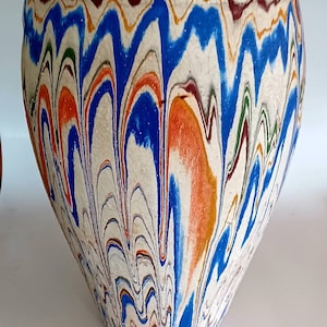 May include: A white ceramic pot with a marbled design in shades of blue, orange, green, and brown. The pot has a rounded shape and a wide opening.