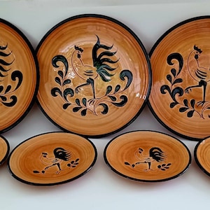 May include: Set of six ceramic plates featuring a black rooster design on a tan background. The plates are in various sizes, with three larger plates and three smaller plates.
